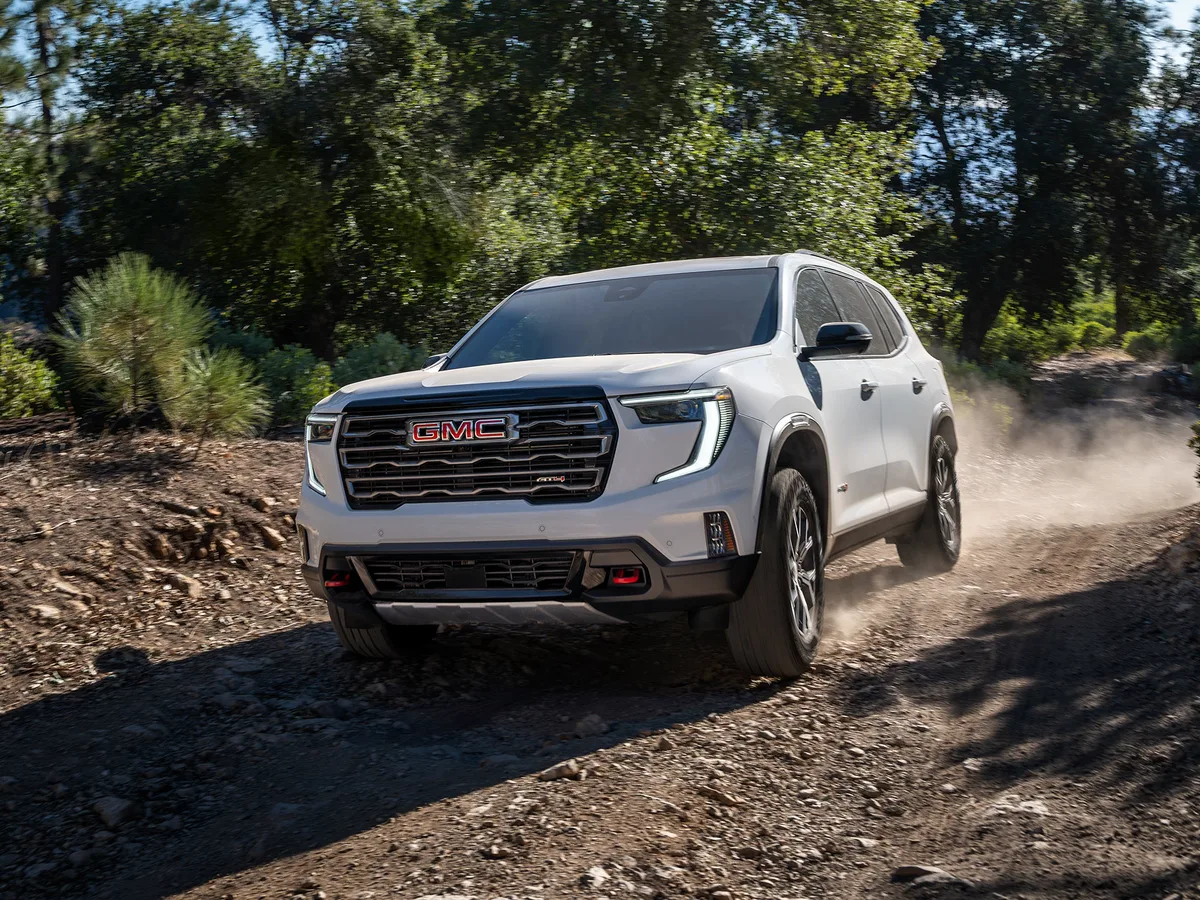 A White 2026 GMC Acadia Mid-Size SUV Parked Driving Down a Dirt Path Between Trees