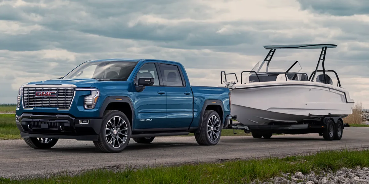 A Blue 2027 GMC Sierra 1500 Denali Truck Towing a White Boat on a Road under a Cloudy Sky