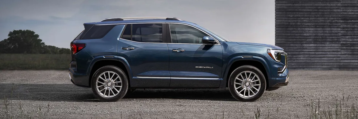 A Side Profile of a Blue GMC Denali SUV Parked on a Gravel Surface next to a Wooden Structure